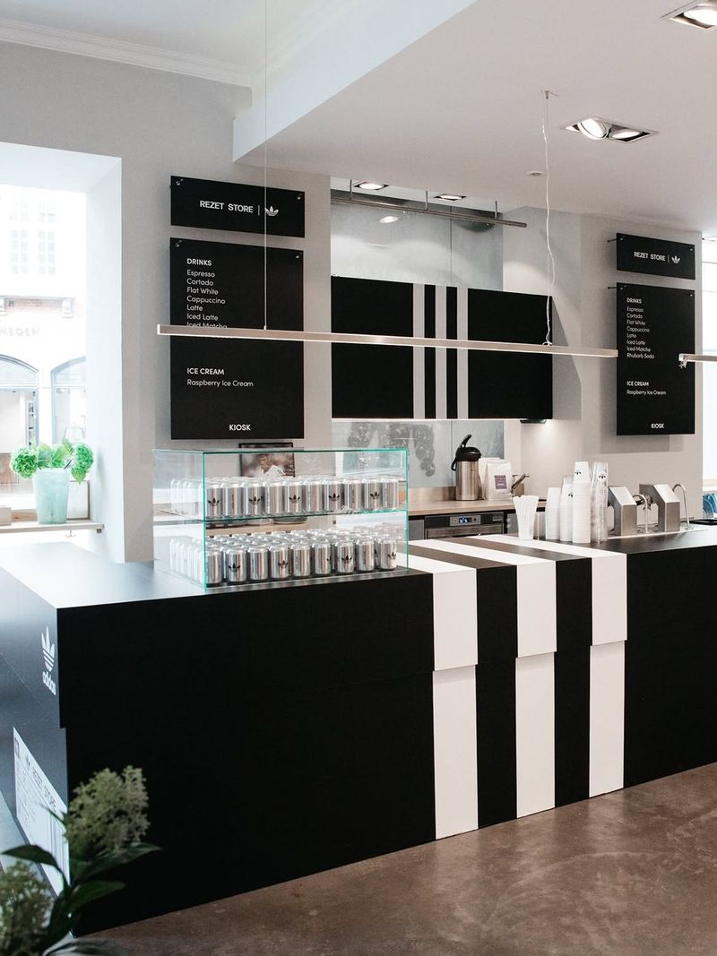 The striped kiosk counter with a glass cabinet of drink cans and hanging menu boards for drinks and ice cream.