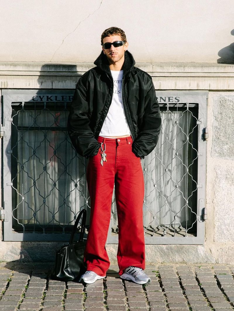 A man in a black puffer jacket and red trousers wearing silver Adistar Control 5 sneakers.
