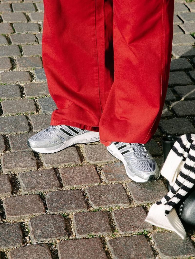 Close-up of silver Adistar Control 5 sneakers under wide red trousers on cobblestones.