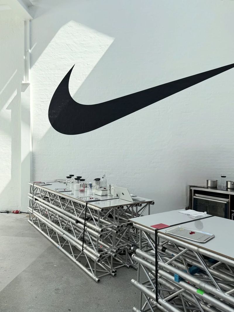 A large black Swoosh on a white wall above a metal truss counter in a Nike activation space.