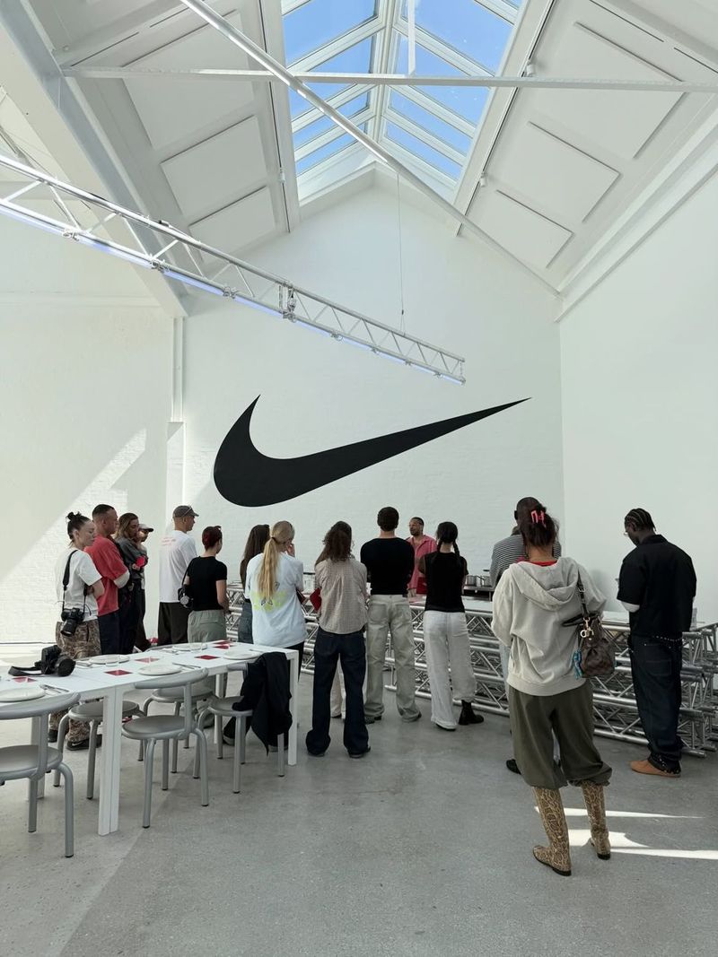 Guests gather under a skylight in a white Nike activation space with a large black Swoosh on the wall.